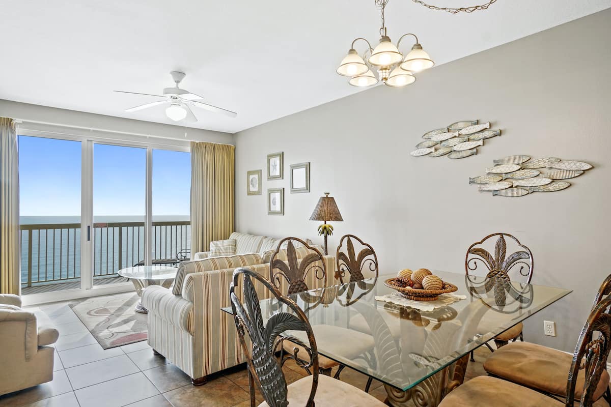 A spacious living area with a balcony, a dining table with chairs, and a ceiling fan.