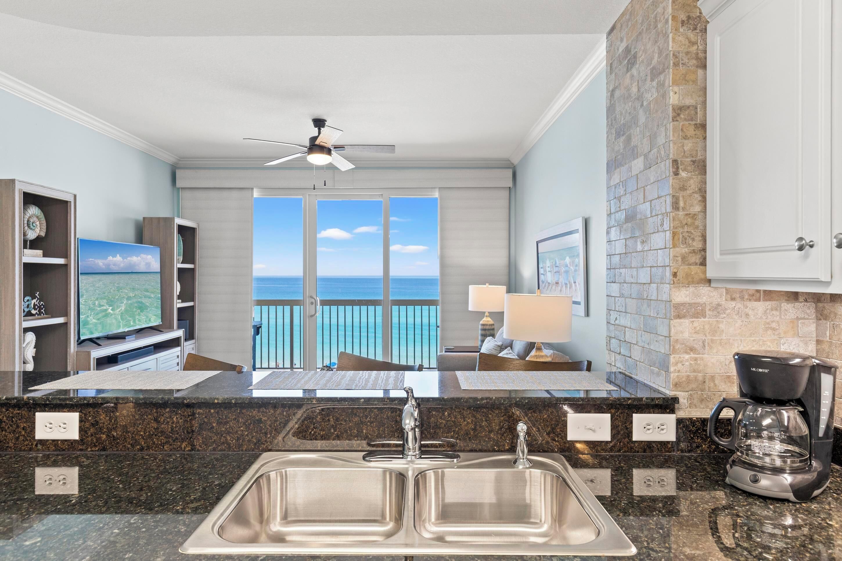 A kitchen with a large sink, a coffee maker, and a view of the ocean.