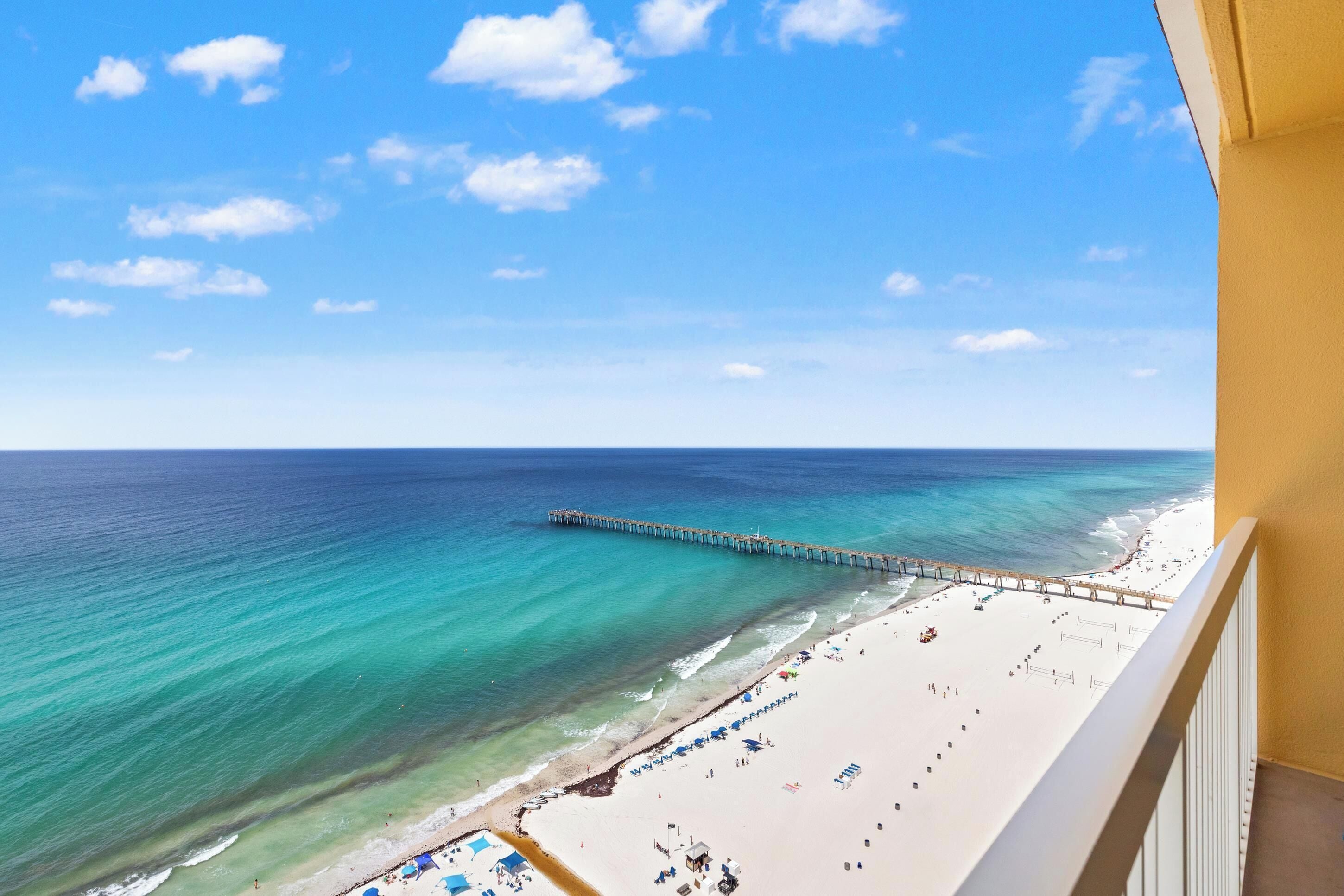 Vista de una playa con un muelle que se adentra en el océano, una playa de arena y un cielo despejado.