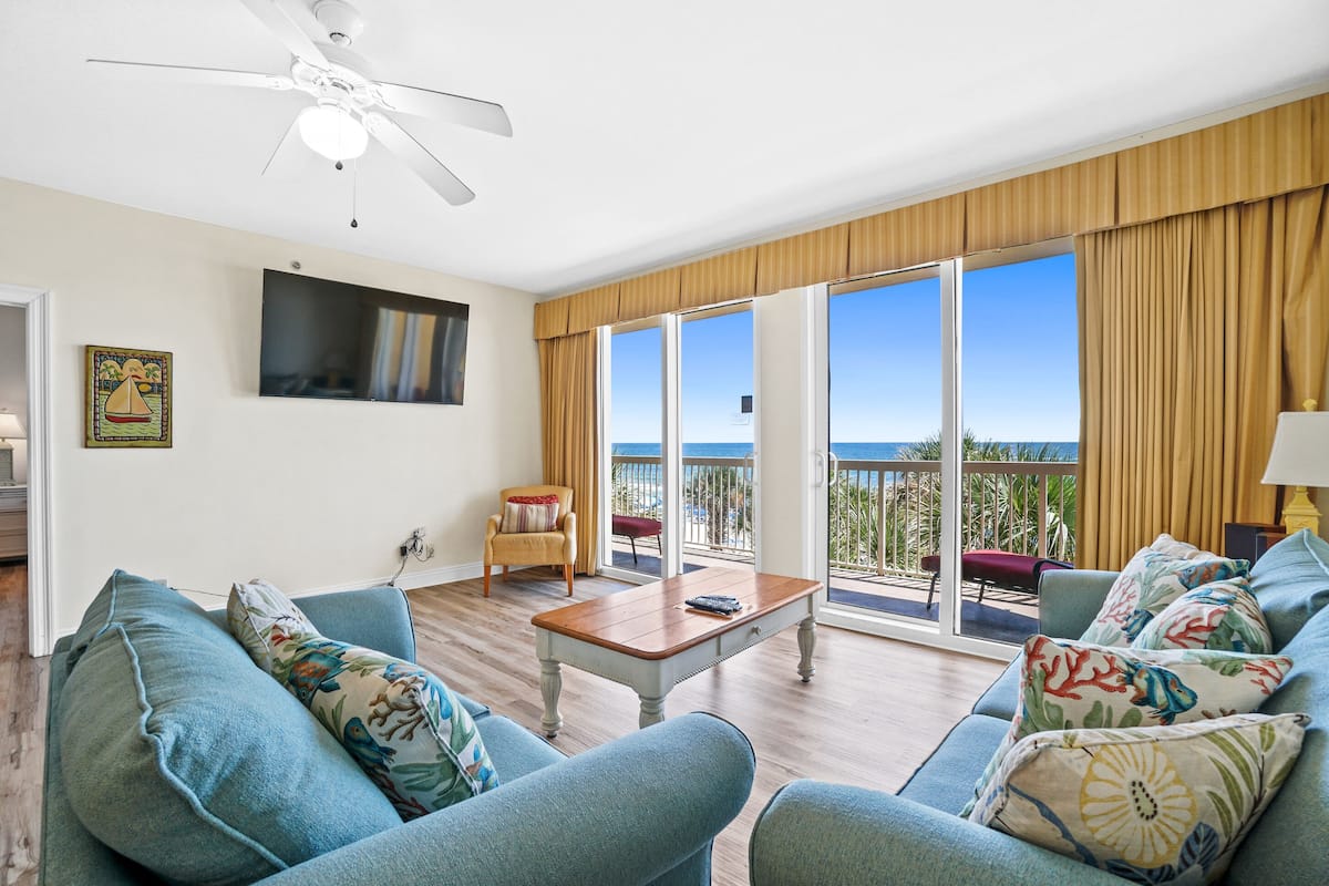 A living room with a large window, a ceiling fan, and a view of the ocean.