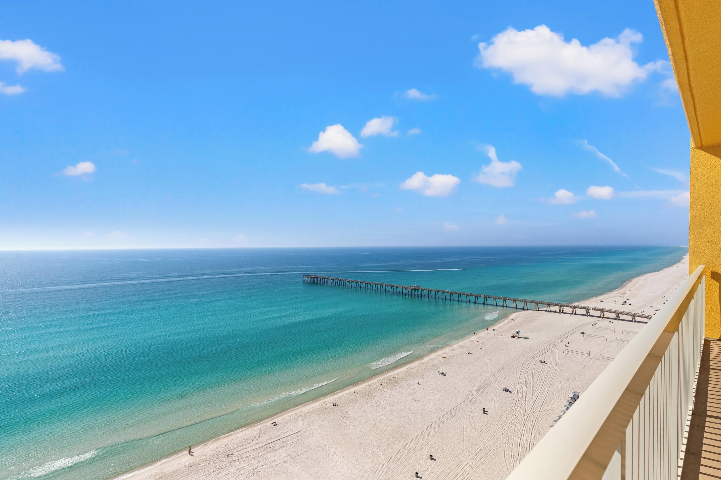Une plage avec une jetée qui s’avance dans l’océan, un ciel dégagé et une rive sablonneuse.