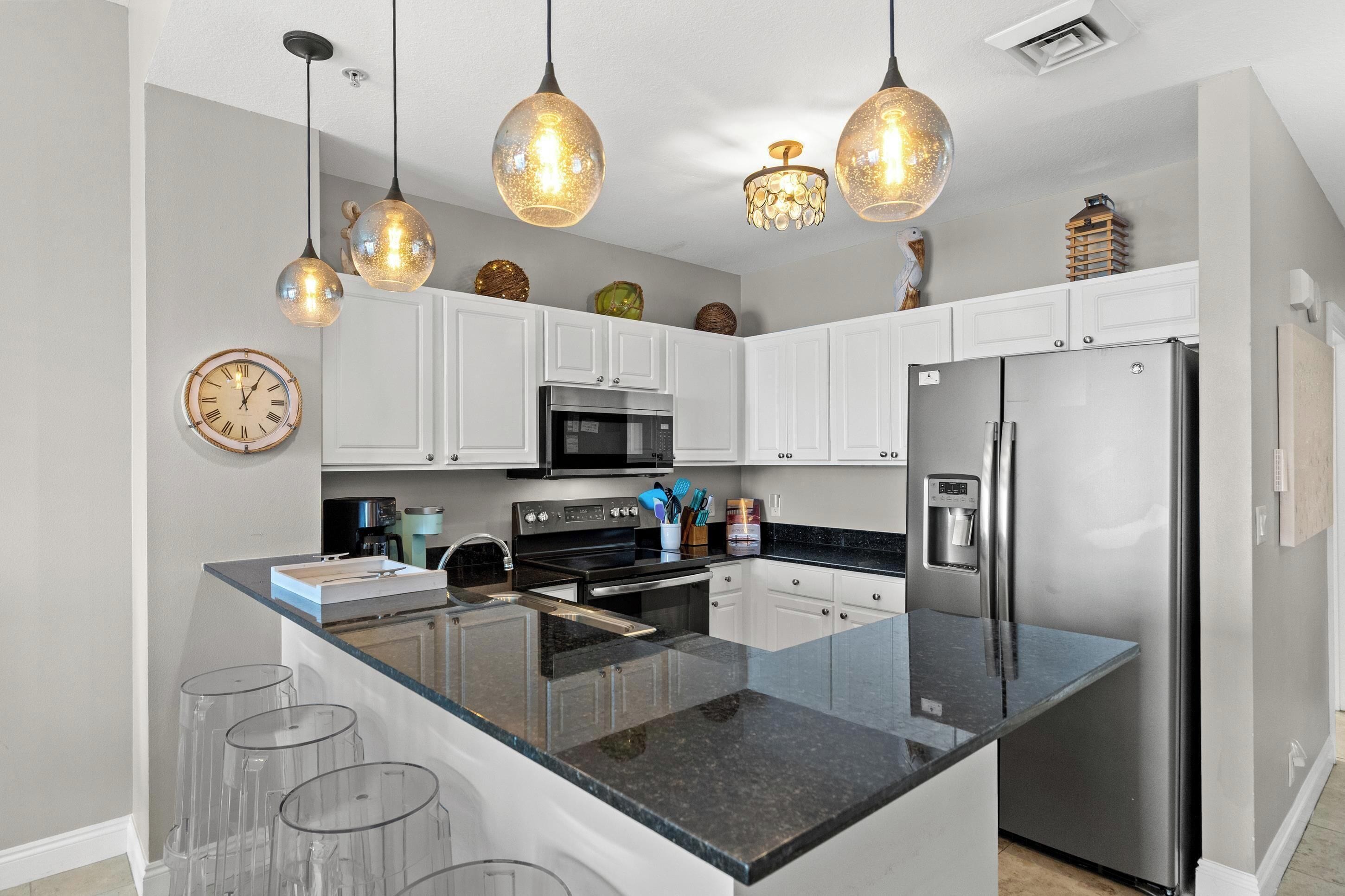 A modern kitchen with white cabinets, a stainless steel refrigerator, a microwave, and a large island with bar stools.
