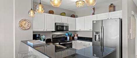 A modern kitchen with white cabinets, a stainless steel refrigerator, a microwave, and a large island with bar stools.