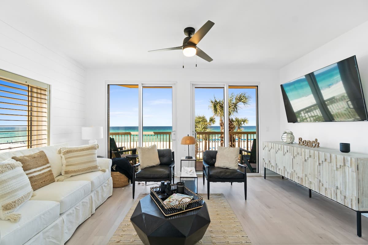 A modern living room with a white sofa, two black chairs, a coffee table, and a TV on the wall.