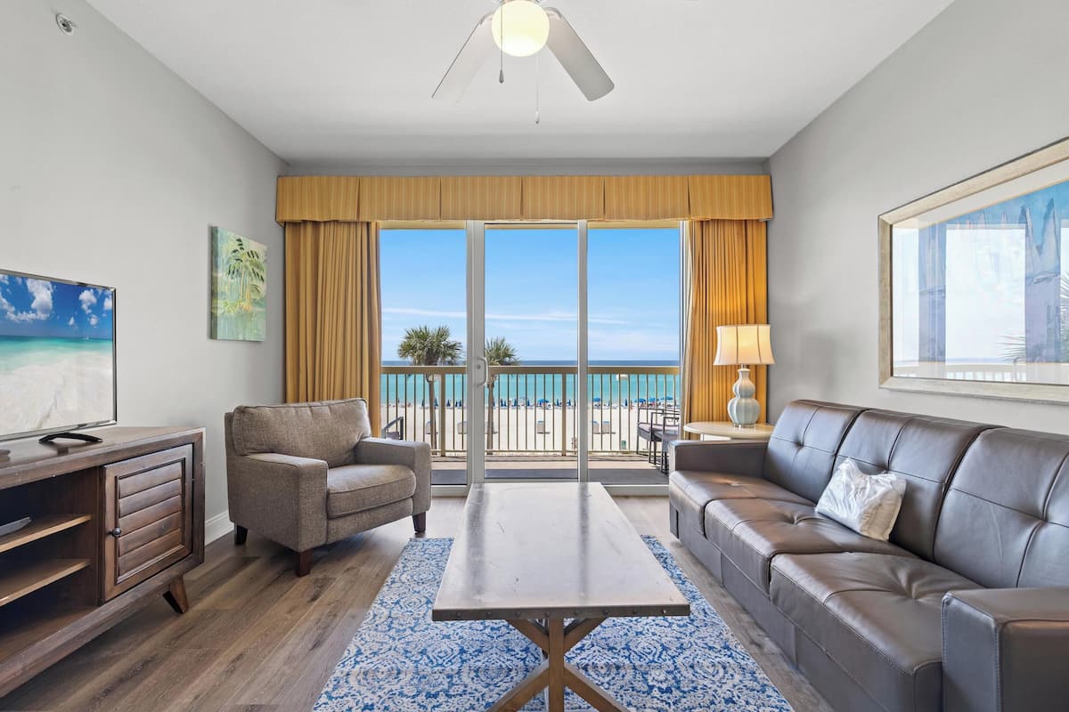 A hotel room with a balcony, a sofa, a coffee table, and a TV.