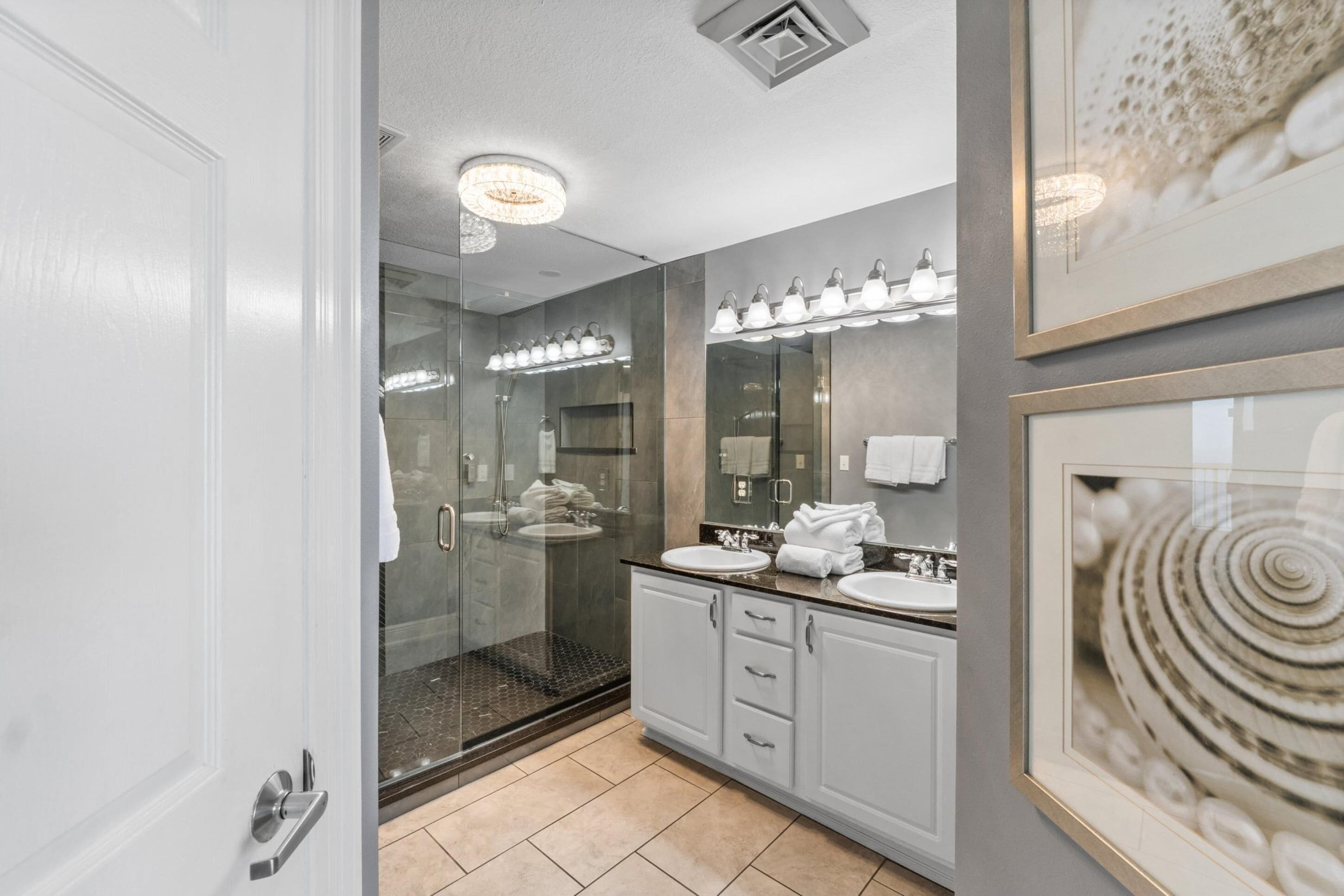 Une salle de bain moderne avec une douche à l’italienne en verre, deux lavabos et un grand miroir.