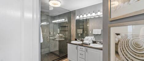 Une salle de bain moderne avec une douche à l’italienne en verre, deux lavabos et un grand miroir.