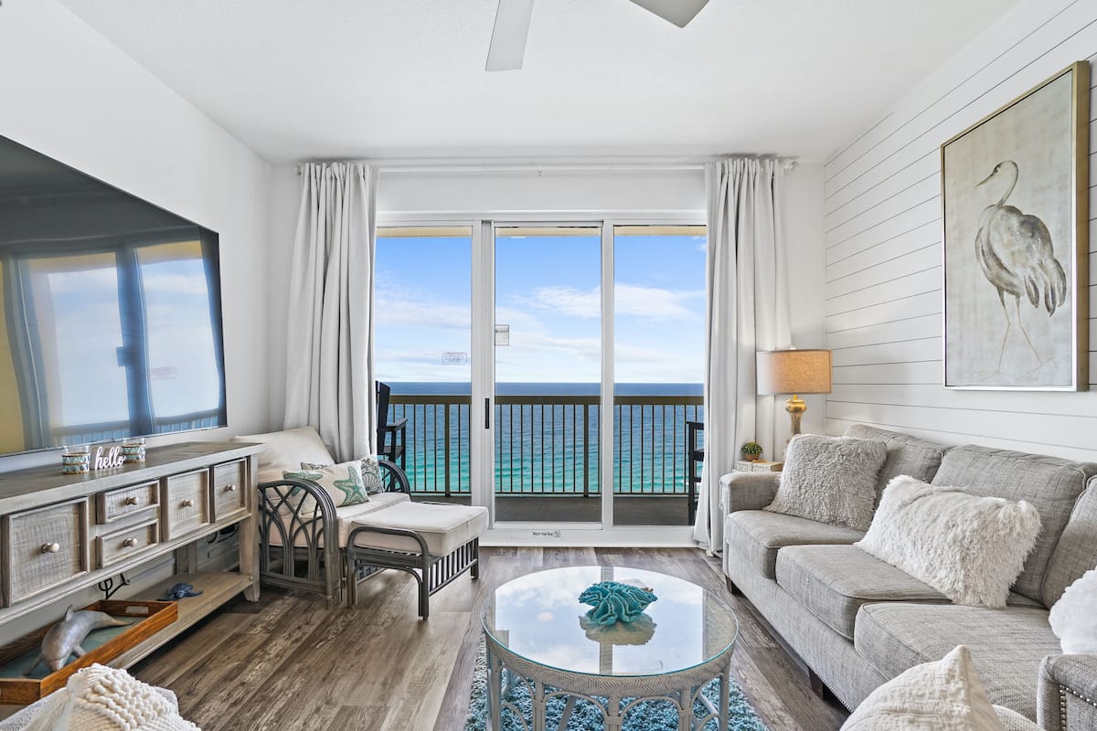 A living room with a view of the ocean, a sofa, a coffee table, and a TV.