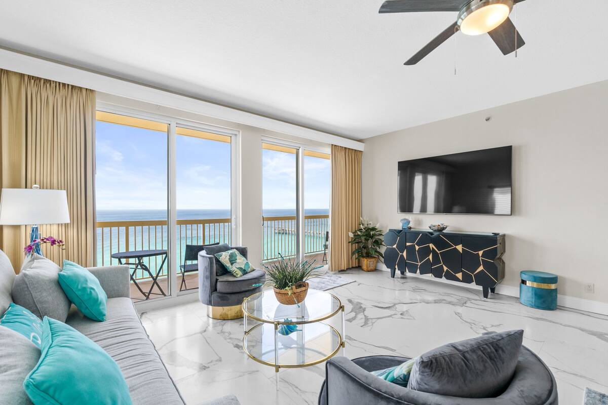 A spacious living room with a large sofa, a round coffee table, and a television mounted on the wall.