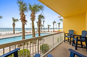 A balcony with a pool, chairs, and a view of the beach and ocean.