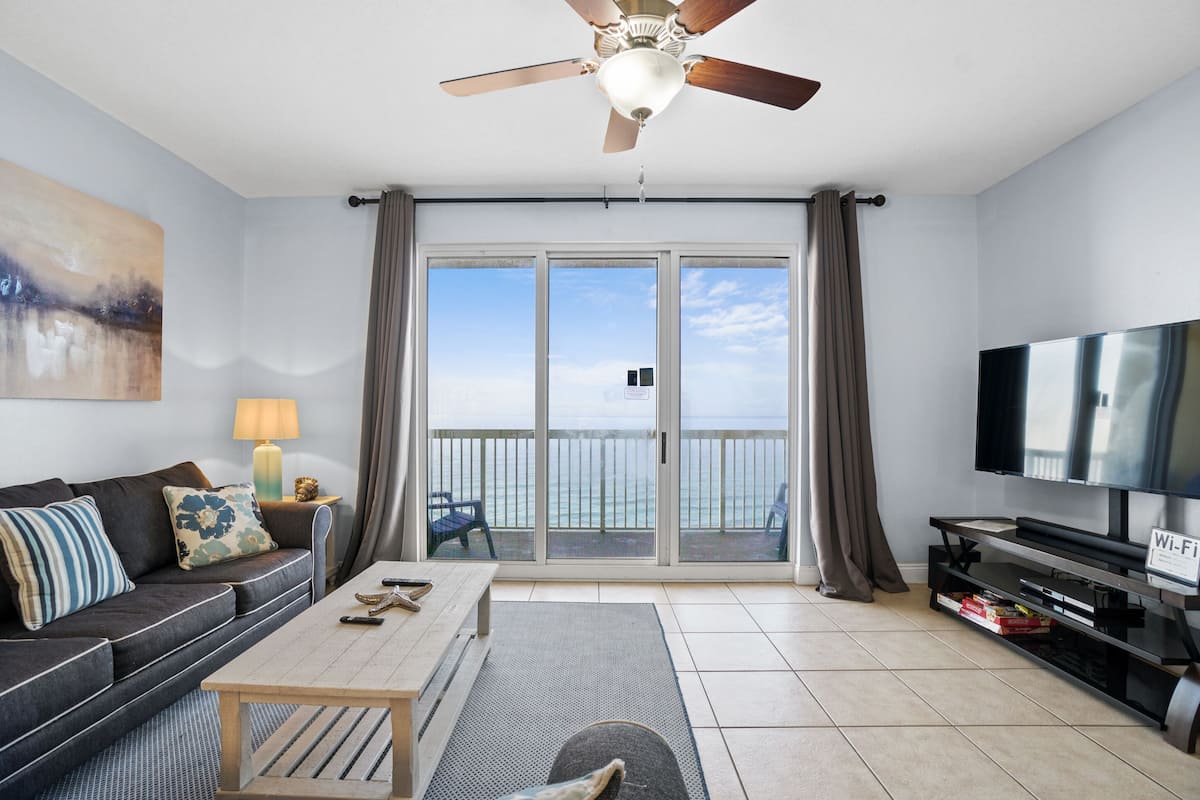 A living room with a sofa, coffee table, TV, and a balcony with a view.