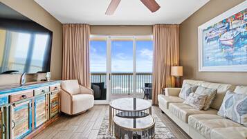 A spacious living room with a large window, a ceiling fan, a sofa, a coffee table, and a TV.