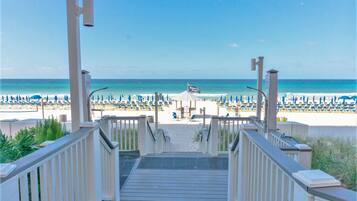 Une vue sur la plage depuis une terrasse en bois, avec en arrière-plan l’océan et des parasols de plage.