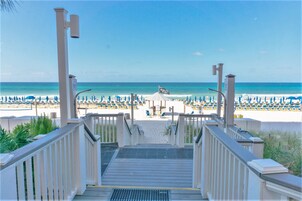A beach view from a wooden deck with a view of the ocean and beach umbrellas.