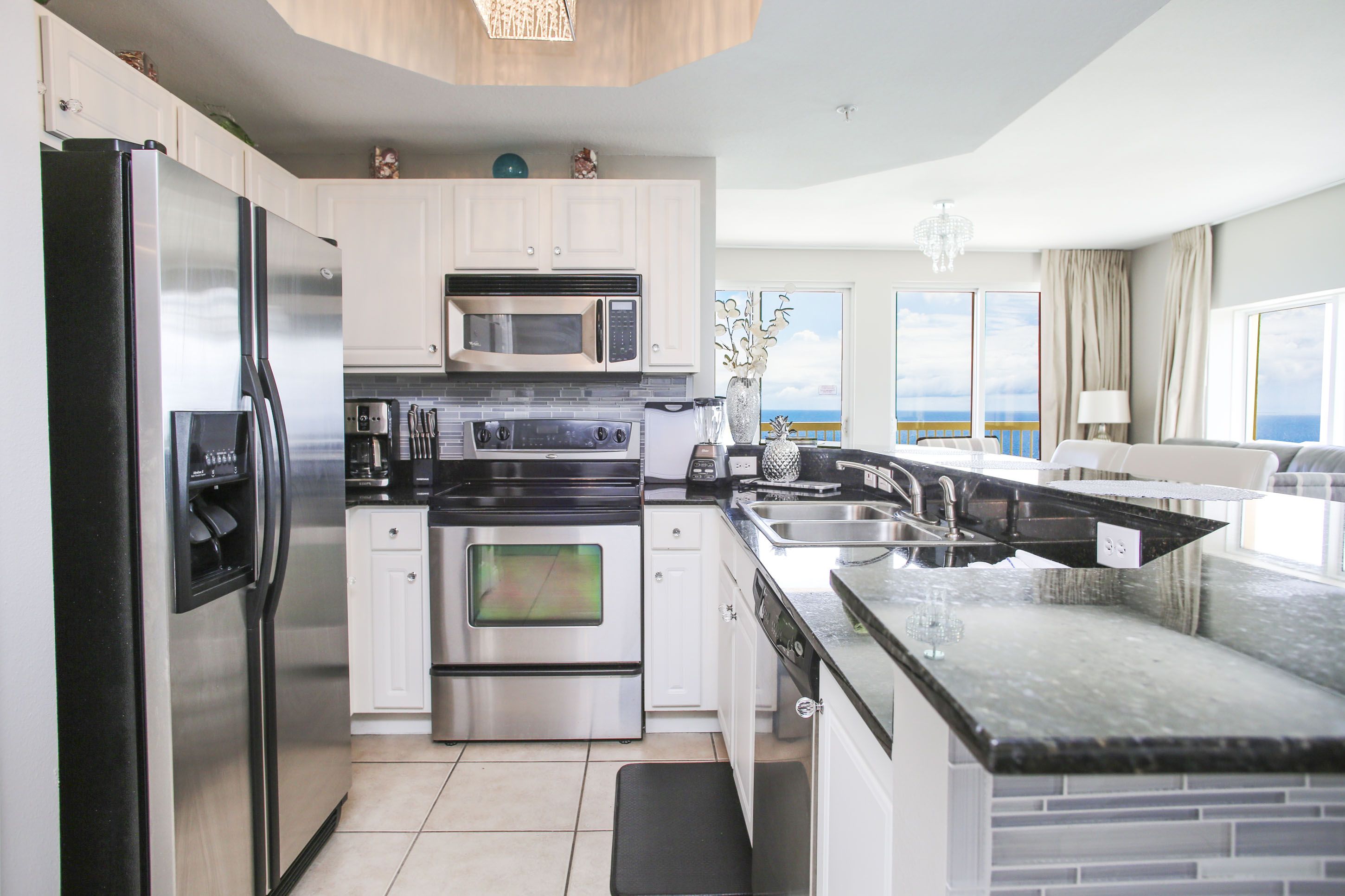 Una cocina moderna con electrodomésticos de acero inoxidable, una isla grande con un fregadero y vistas al océano a través de las ventanas.