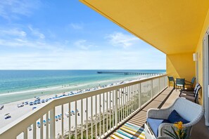 Varanda com vista para a praia e o cais, mobiliário de vime e toldo amarelo.