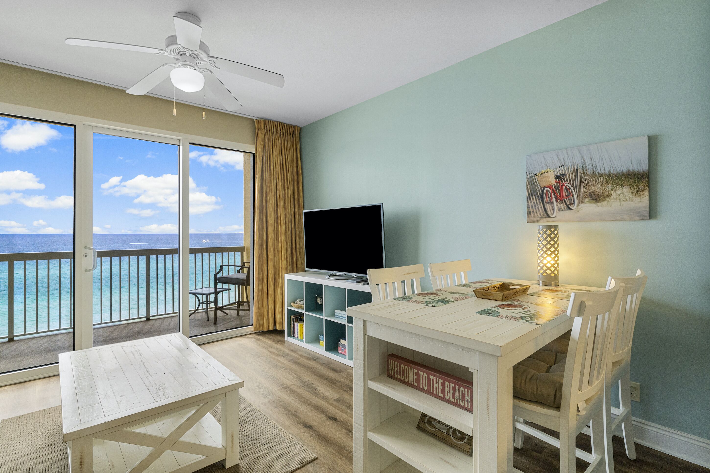 A room with a balcony, a TV, a dining table, and a painting.