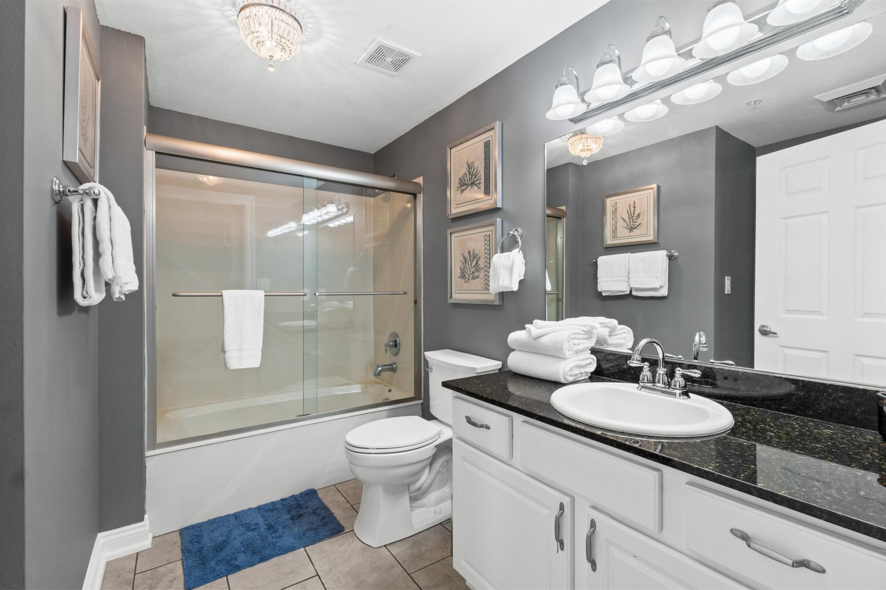 Un baño moderno con cabina de ducha de vidrio, inodoro blanco, tocador con encimera negra y un espejo grande.