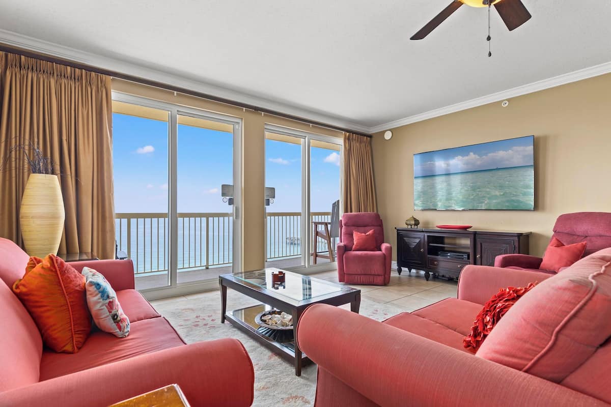 A living room with a sofa, armchairs, a coffee table, a TV, and a balcony with a view.