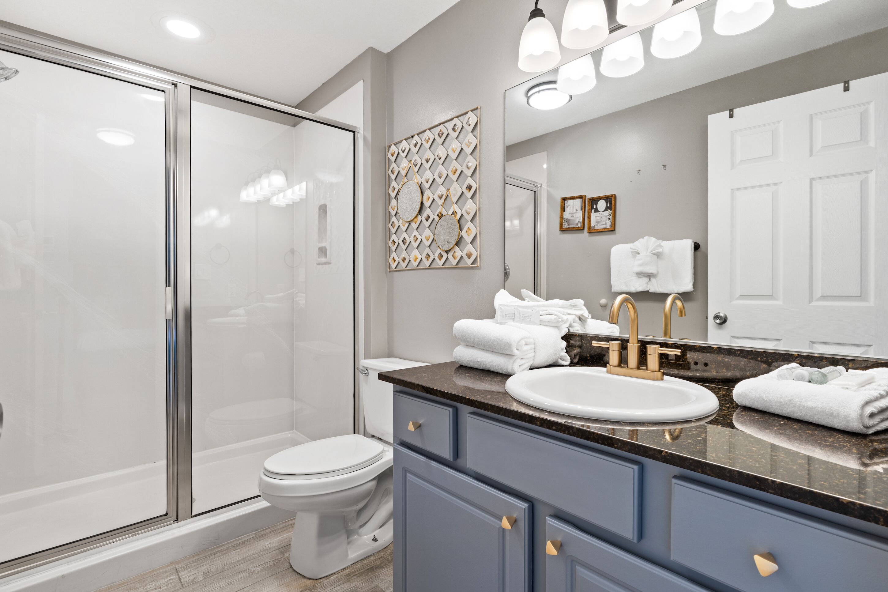 A modern bathroom with a glass shower enclosure, a white toilet, a sink with a gold faucet, and a large mirror.