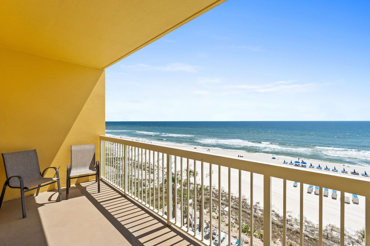 A balcony with two chairs, a view of the beach, and a railing.