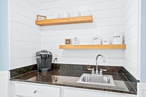 A kitchen with a coffee maker, a sink, and shelves with labeled containers for coffee, tea, and sugar.