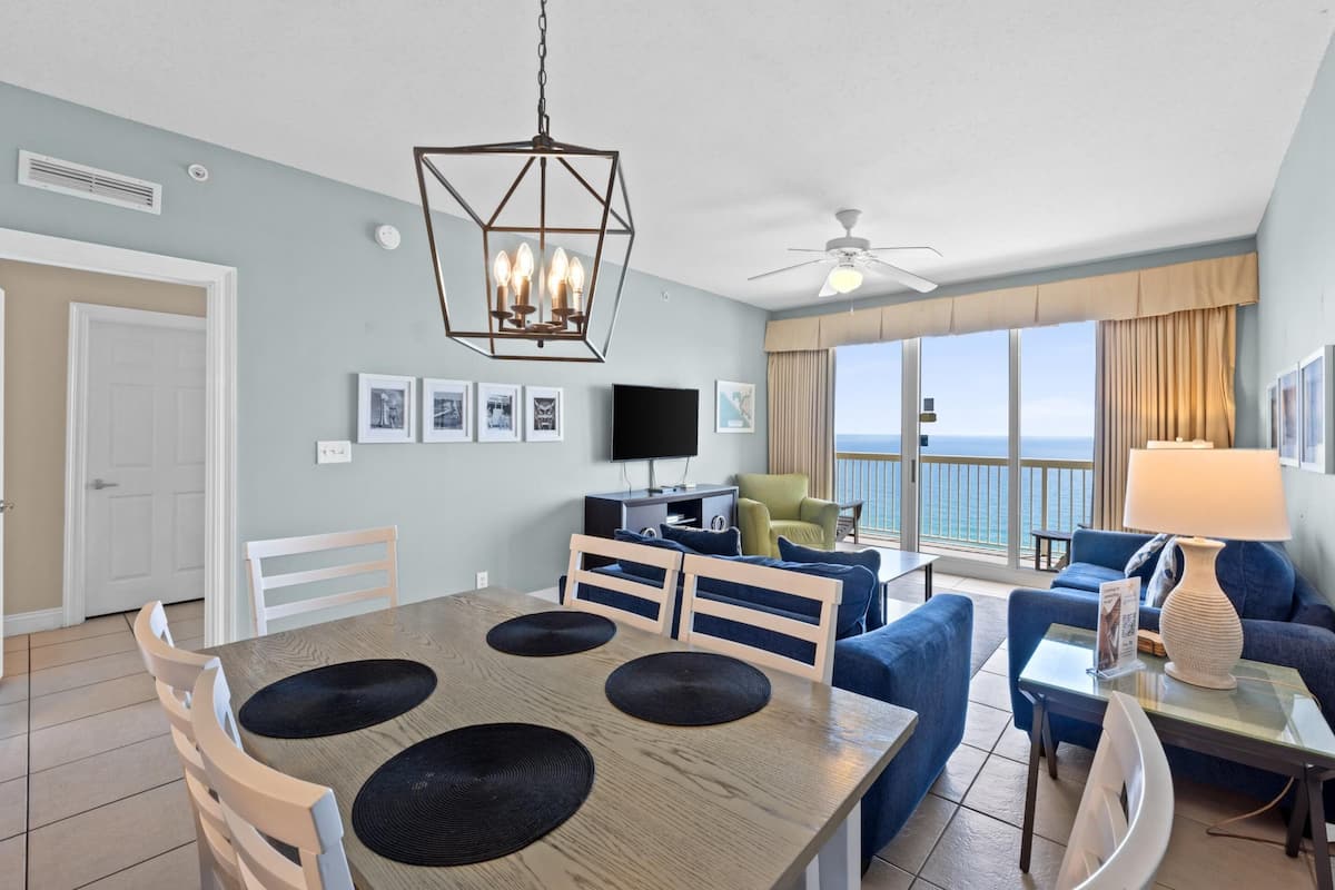 A modern living room with a dining area, a flat-screen TV, and a view of the ocean.