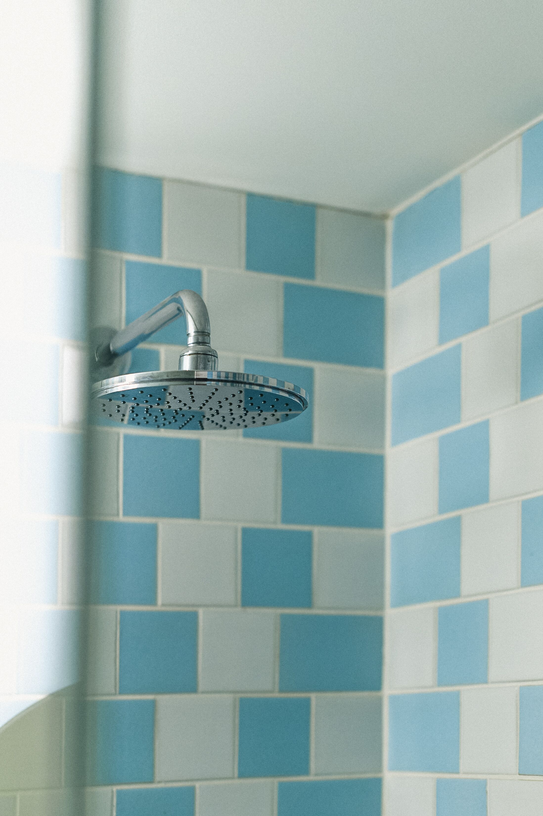 A showerhead with a curved design, mounted on a wall with blue and white tiles.