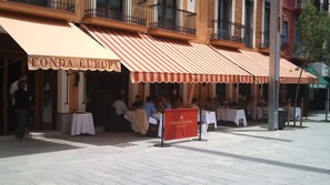 Un área de comedor al aire libre de Fonda Europa con mesas y sillas, un toldo rojo y un letrero.