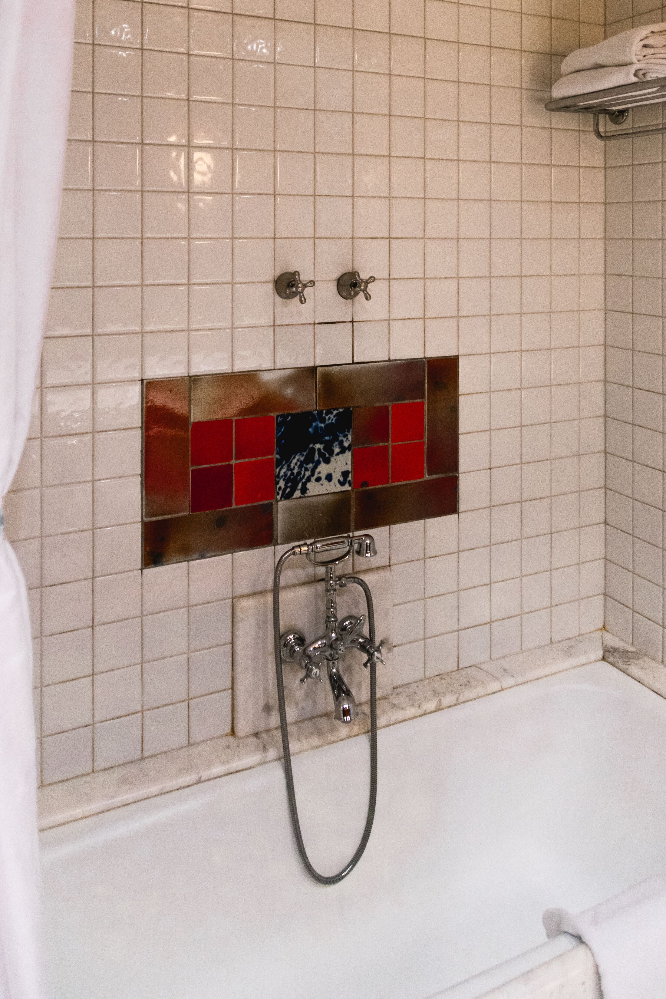 A bathroom with a bathtub, a shower, and a tiled wall with a decorative tile panel.