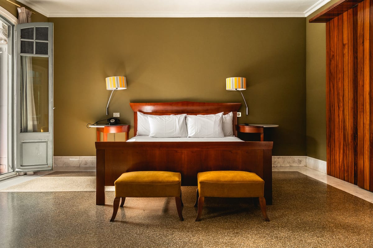 A bedroom with a wooden bed, two bedside lamps, and two matching ottomans.