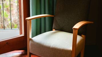 Ein Stuhl mit Holzauflagen an den Armlehnen und einem gepolsterten Sitz in einem Zimmer mit Holzboden und einem Fenster mit grünen Vorhängen.