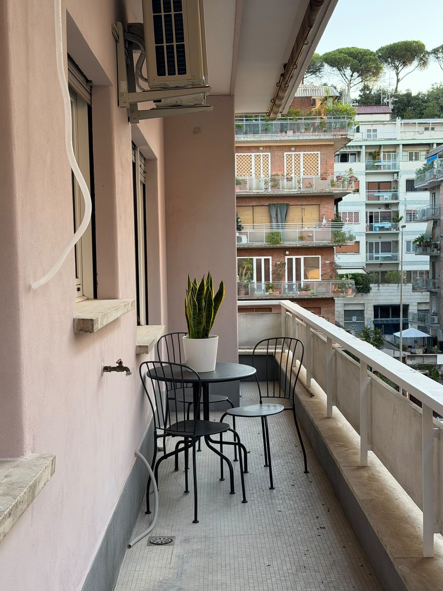 A balcony with a table and chairs, a potted plant, and a view of a residential building.