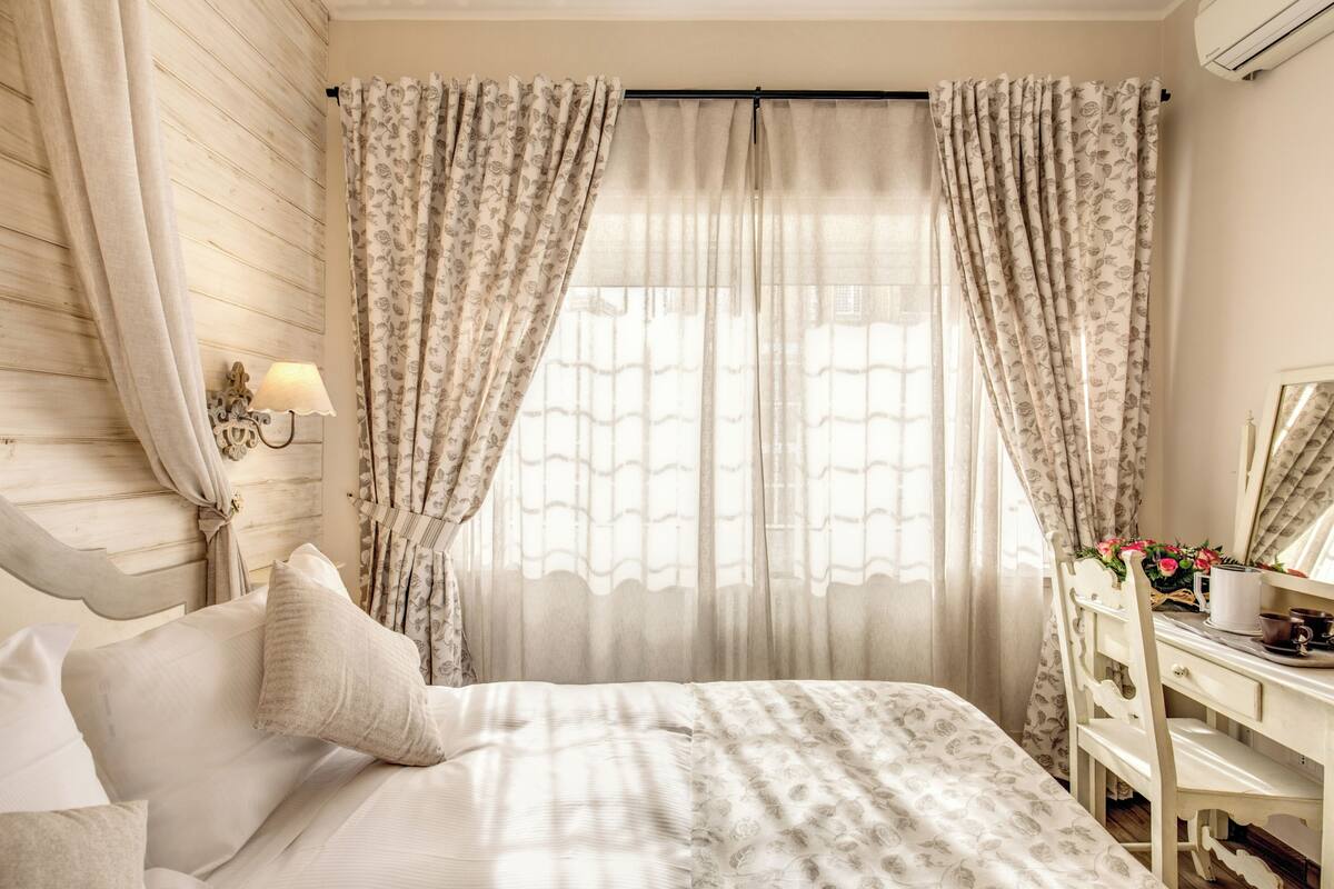 A bedroom with a bed, curtains, a desk, a lamp, and a mirror.