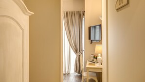 A hotel room with a bed, a desk with a lamp, a TV, and a window with curtains. - Casa Mia Vaticano Guest House (Rome)