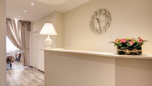 A reception area with a clock, a lamp, and a flower arrangement on a counter. - Casa Mia Vaticano Guest House (Rome)
