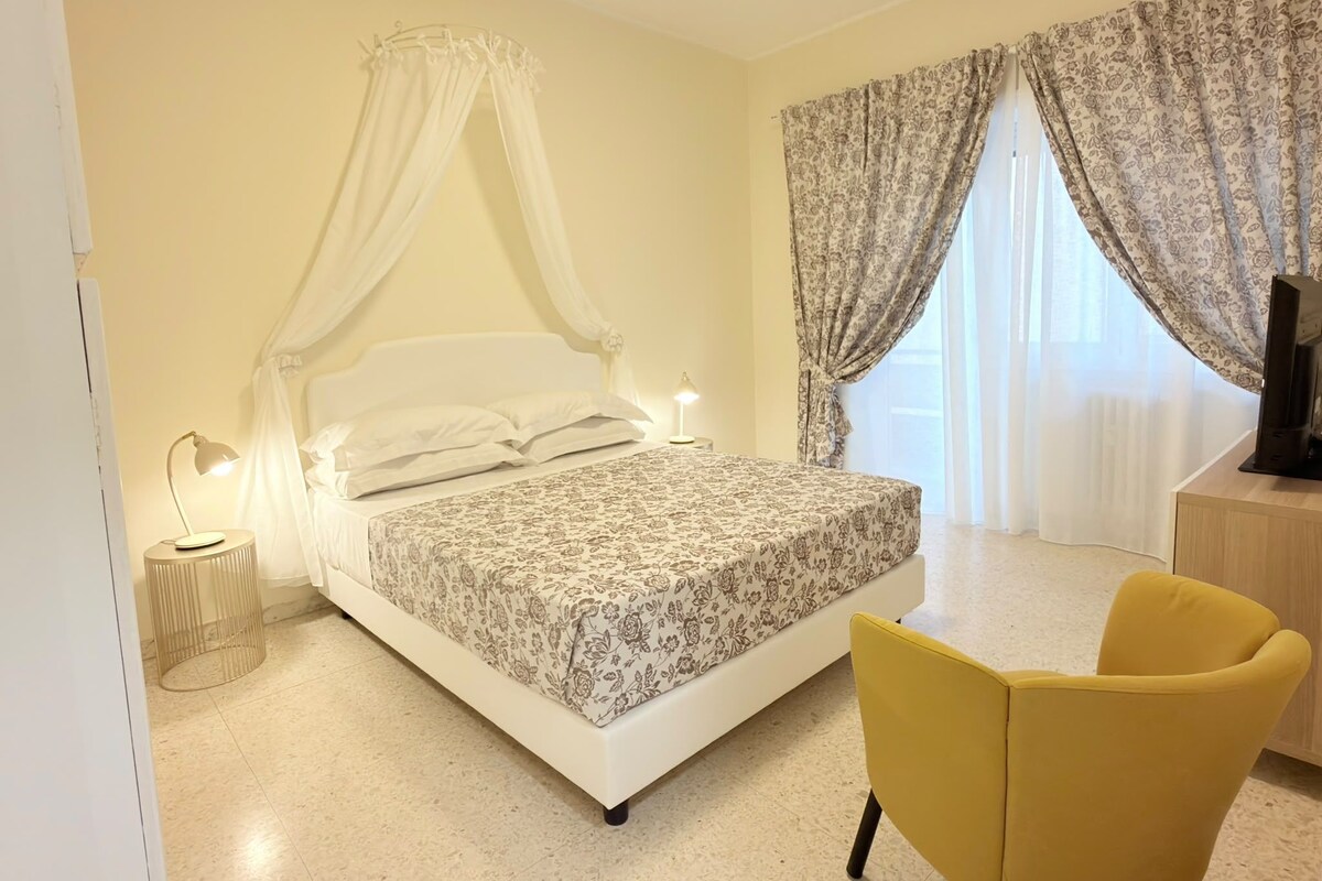 A bedroom with a bed, a bedside lamp, a chair, and curtains.