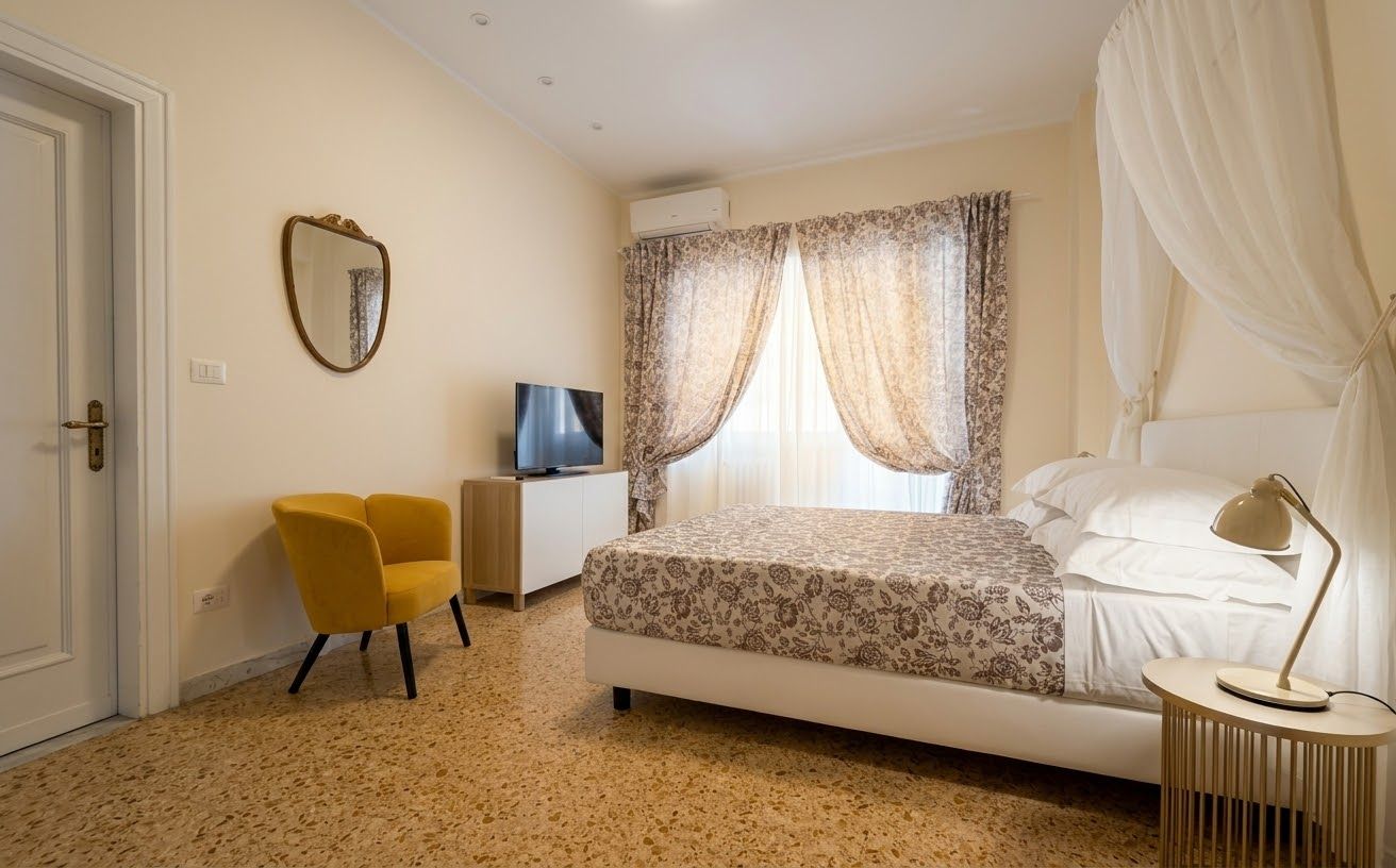 Une chambre à coucher avec un lit, une chaise, un bureau, un téléviseur et une fenêtre avec des rideaux.
