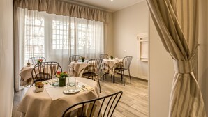 A dining area with tables set for two, featuring metal chairs and beige tablecloths. - Casa Mia Vaticano Guest House (Rome)