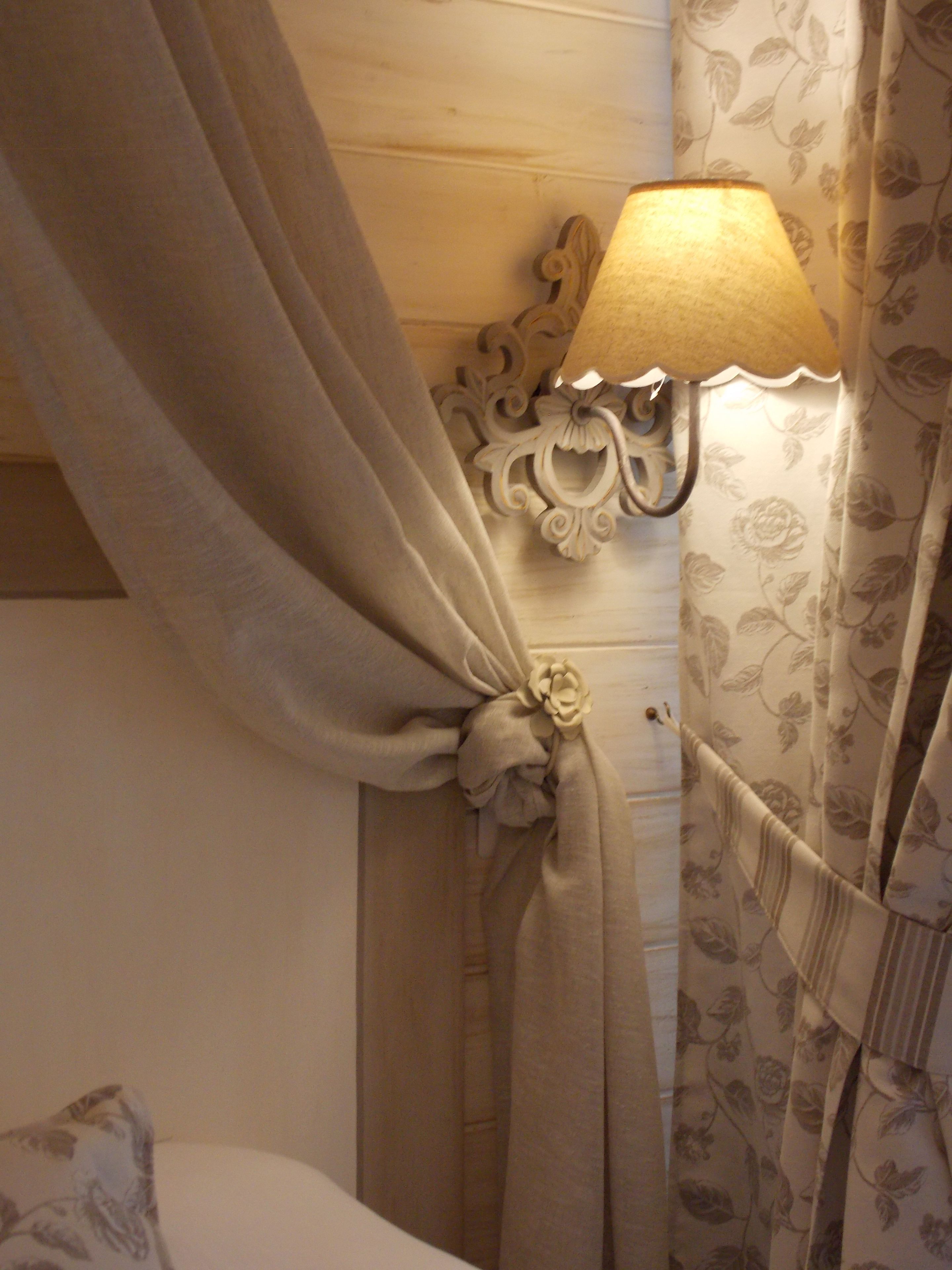 A bed with a headboard, a wall-mounted lamp, and curtains with a floral pattern.