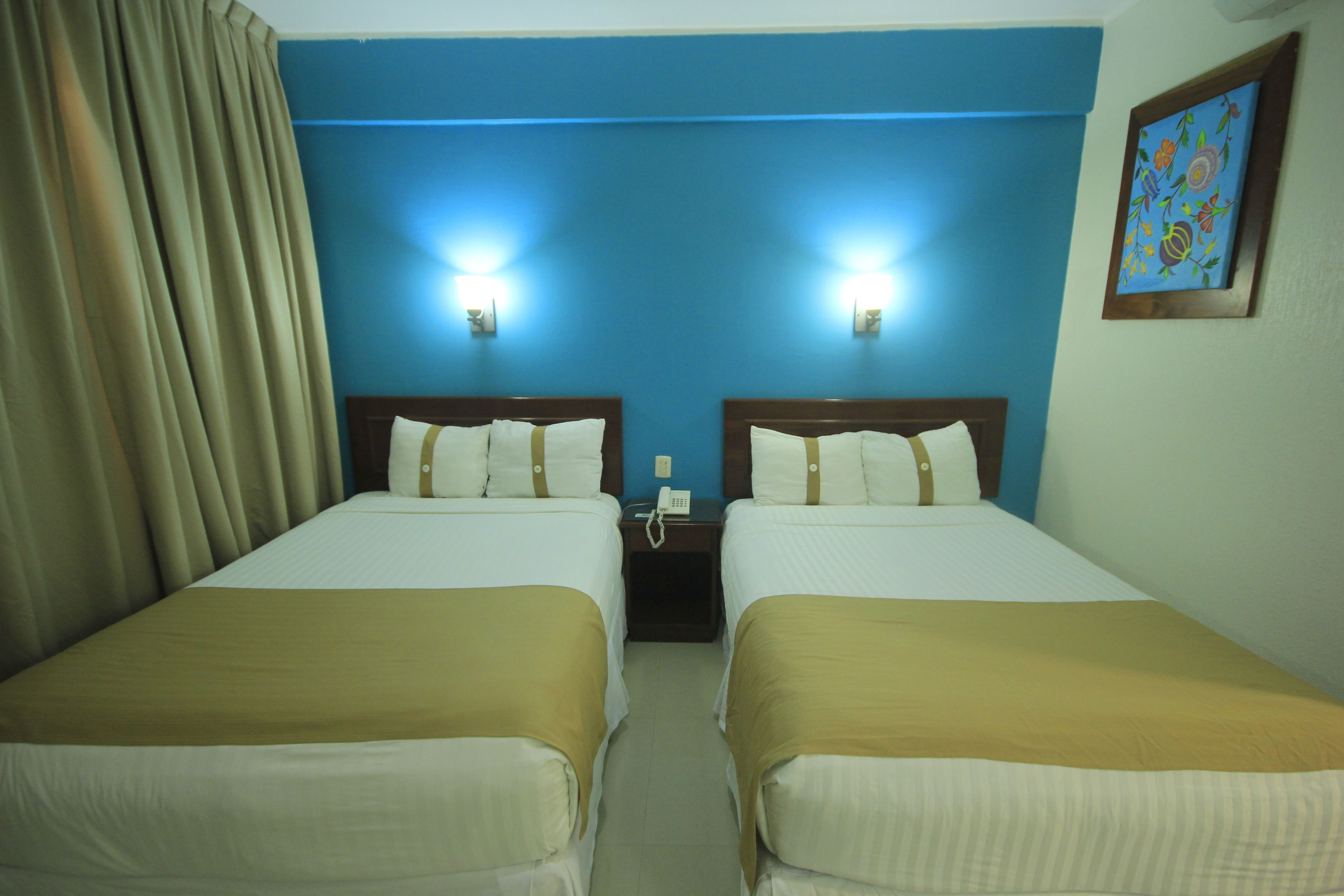Habitación de hotel con dos camas, ropa de cama color beige, un teléfono en la mesita de noche y un cuadro en la pared.