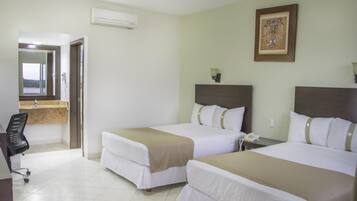 Habitación de hotel con dos camas, un escritorio y un baño visible a través de una puerta abierta.