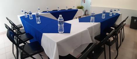 A conference room with tables covered in blue tablecloths, each with a water bottle.