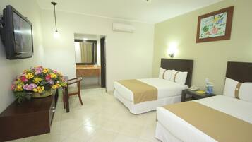 Habitación de hotel con dos camas, un escritorio con televisor, una silla, un baño y una decoración floral.