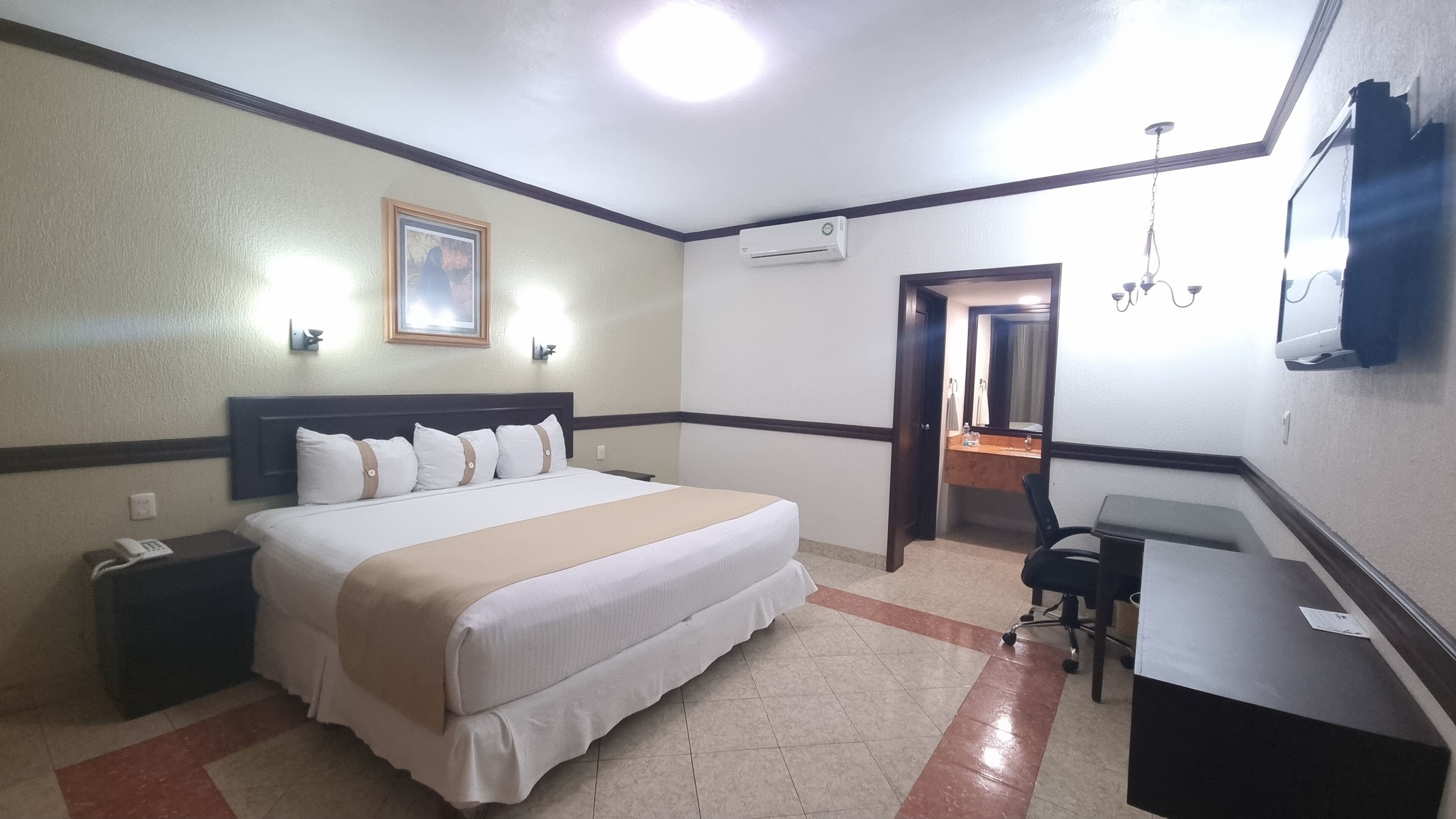 Een hotelkamer met een bed, nachtkastje, bureau, stoel en een airconditioning.
