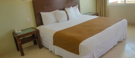 Una habitación de hotel con una cama grande, dos mesitas de noche, un teléfono y dos lámparas de pared.