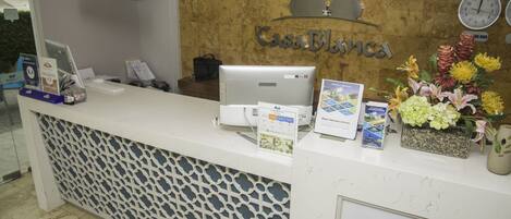 A reception desk with a computer, a clock, and a flower arrangement.