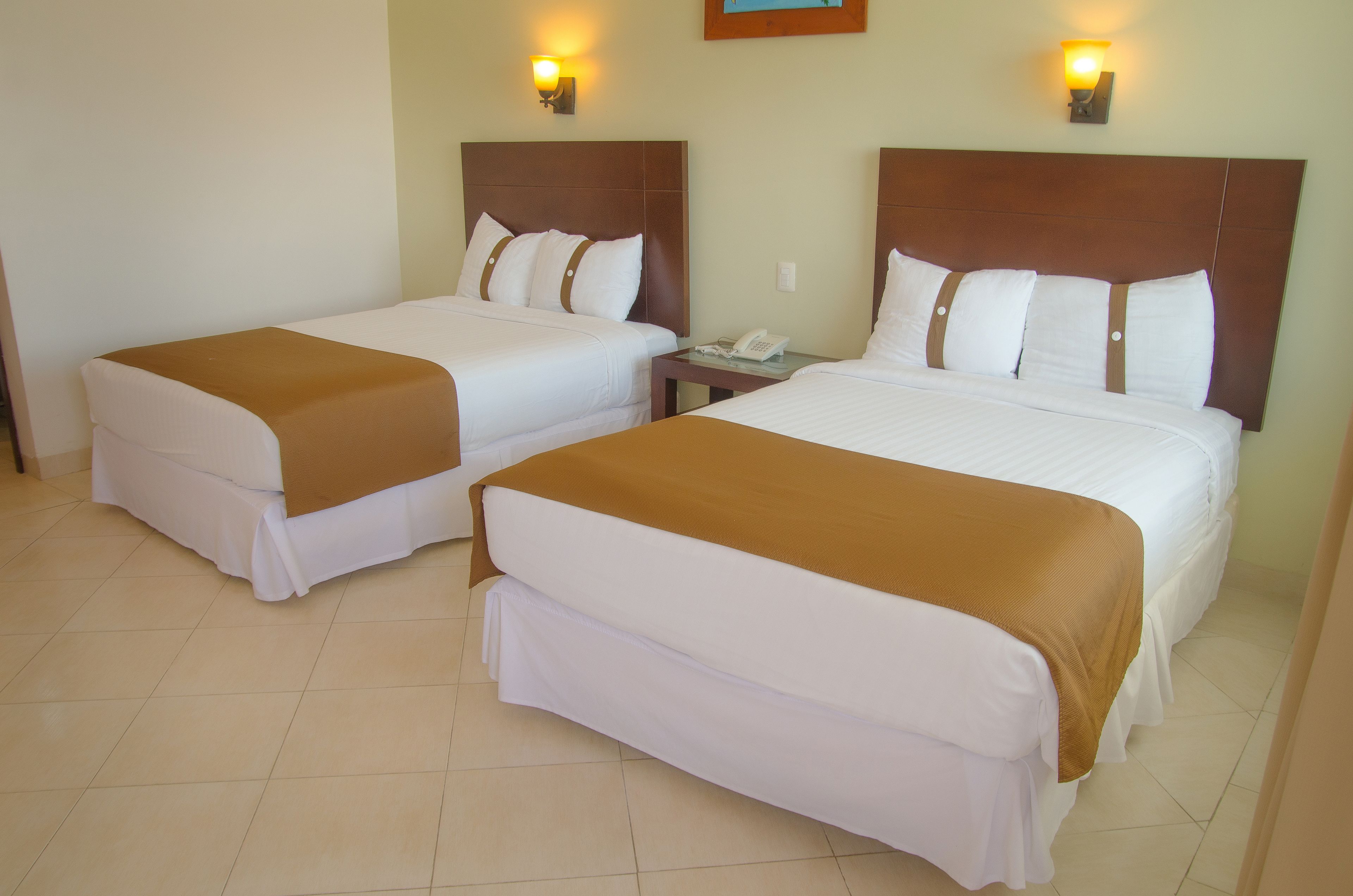 A hotel room with two single beds, each with a brown headboard and white bedding. There is a nightstand with a telephone between the beds.