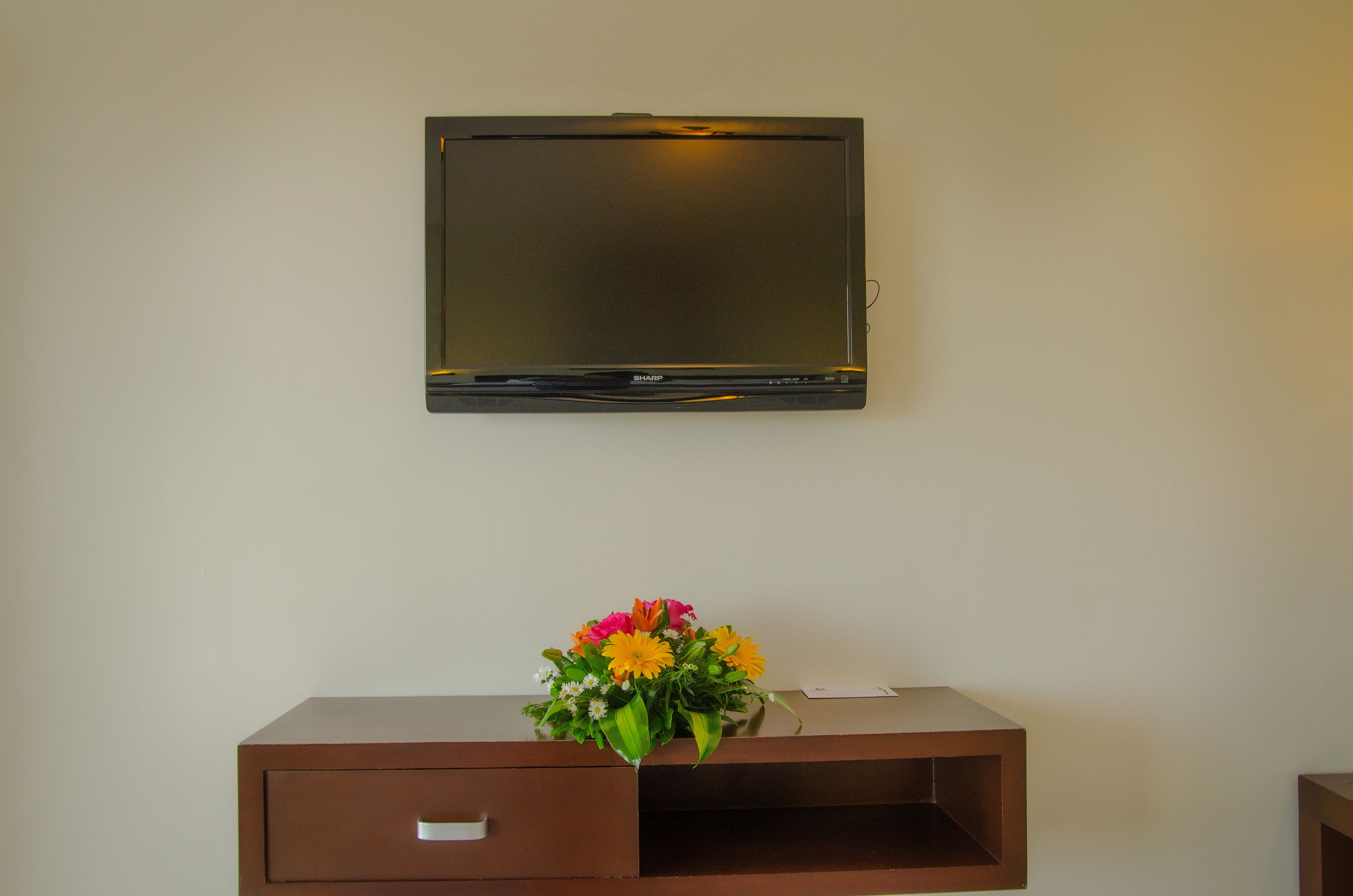 A flat-screen TV mounted on a wall above a wooden console with a floral arrangement.