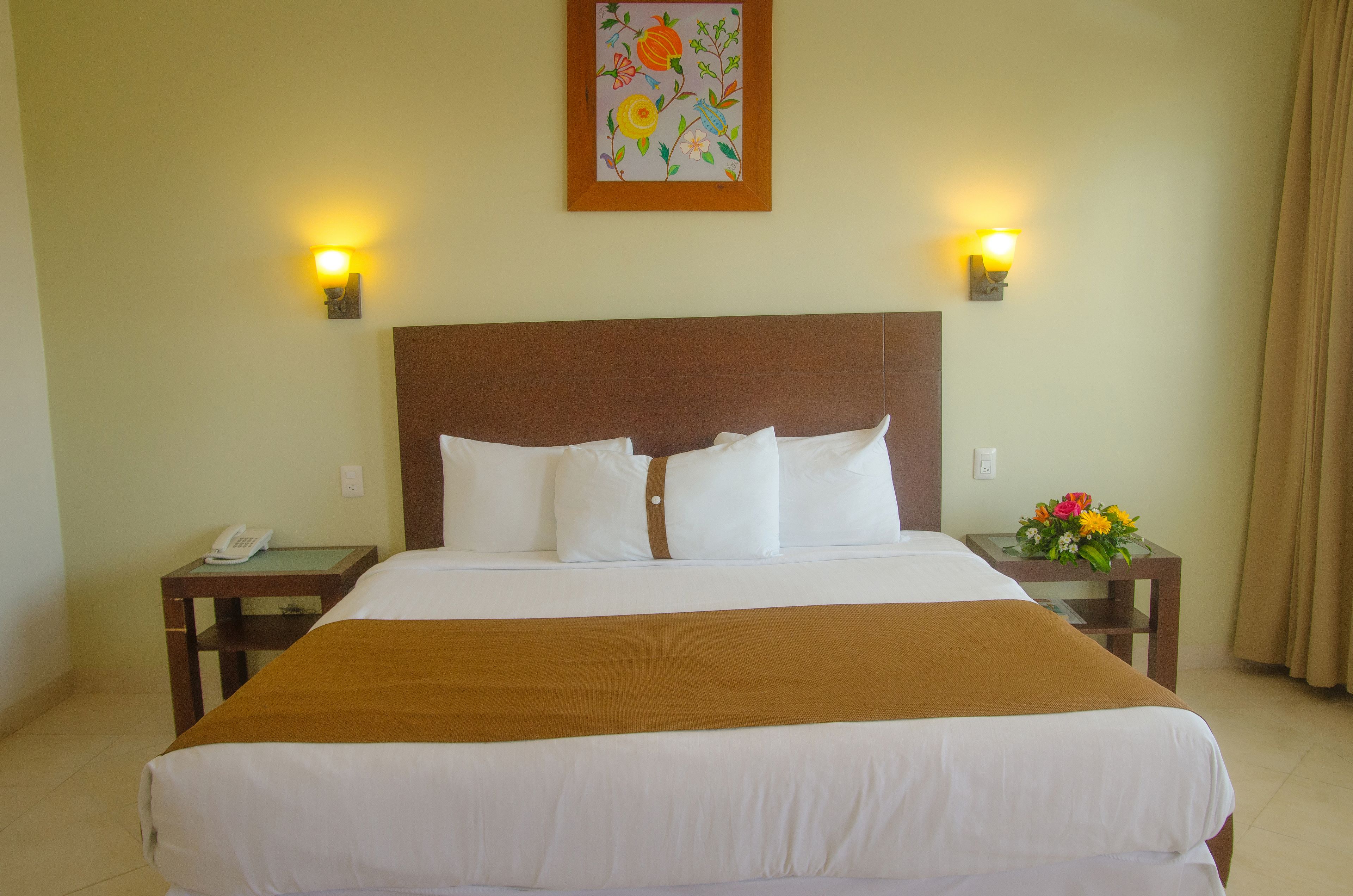 Een hotelkamer met een groot bed, twee nachtkastjes, een telefoon en een bloemen decoratie aan de muur.
